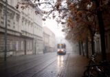 Tramwaj jadący ulicą między kamienicami w deszczowy jesienny poranek w Krakowie